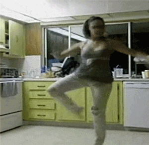 a woman is dancing in a kitchen in front of yellow cabinets