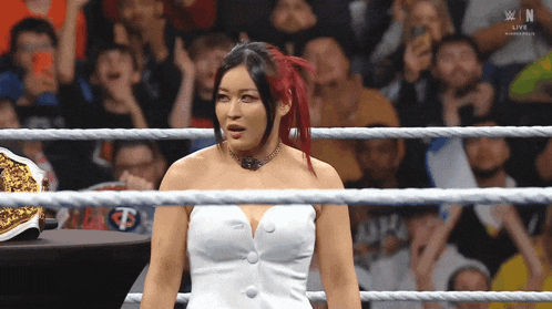 a woman in a white dress is in a wrestling ring with a crowd watching