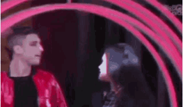 a man in a red jacket and a woman in a black dress are standing next to each other in a pink circle .