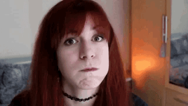 a woman with red hair is making a funny face while wearing a choker .