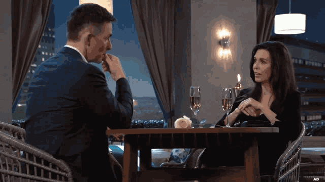 a man and a woman sit at a table with glasses of champagne