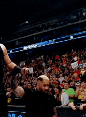 a man in a black vest is standing in front of a crowd in a stadium .