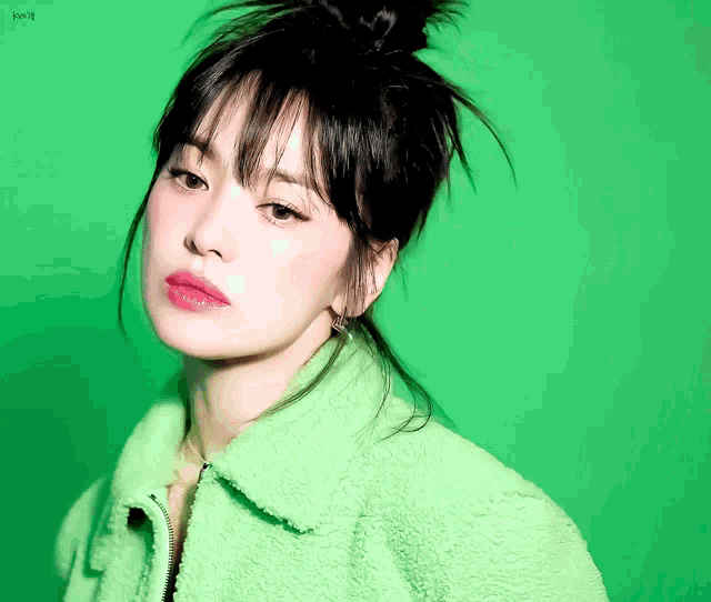 a woman in a green jacket is looking at the camera with a green background