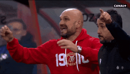 a man wearing a red sweatshirt with the number 19 on it is pointing