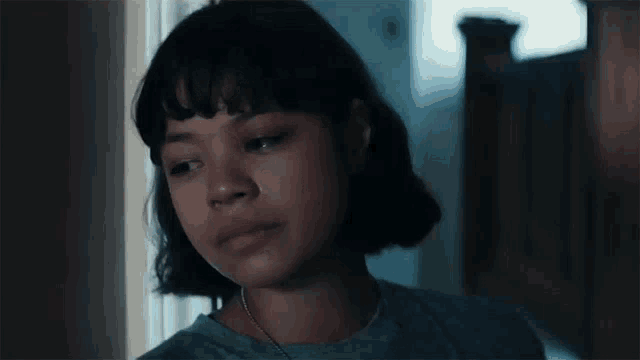 a young girl with short hair and bangs is standing in a dark room looking at the camera .