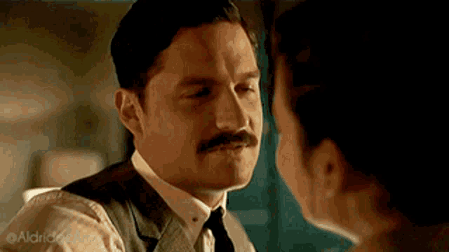 a man with a mustache is kissing a woman on the forehead .