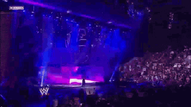 a man in a black tank top is standing in front of a purple wall on a stage .