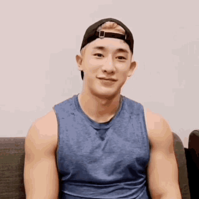 a young man wearing a blue tank top and a baseball cap is sitting on a couch .