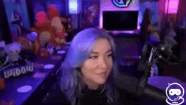 a woman with blue hair is sitting in front of a microphone in a video game room .