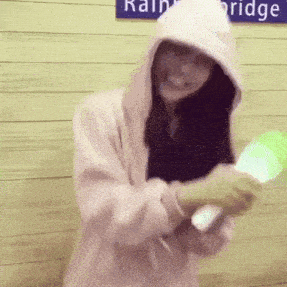 a woman wearing a hoodie is holding a green light stick in front of a sign that says rain bridge