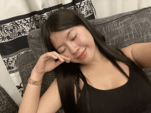 a woman in a black tank top is laying on a couch
