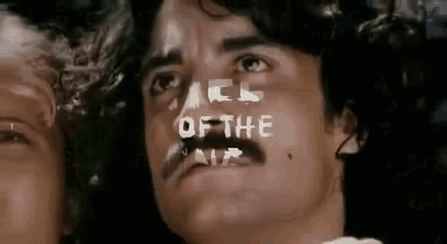 a man with a mustache is looking up at the camera with the words `` face of the air '' written on his face .