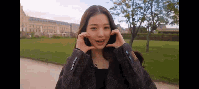 a young woman in a plaid jacket is making a heart shape with her hands .