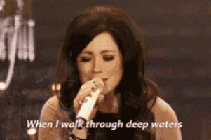 a woman singing into a microphone with the words when i walk through deep waters