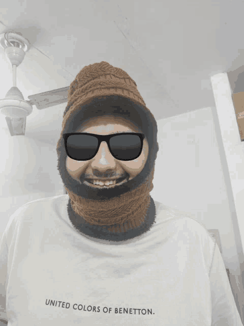 a man wearing sunglasses and a united colors of benetton shirt smiles