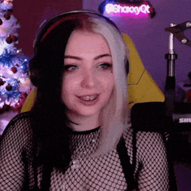 a woman wearing headphones and a fishnet top is smiling in front of a christmas tree .