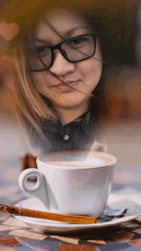 a woman wearing glasses is sitting at a table with a cup of coffee