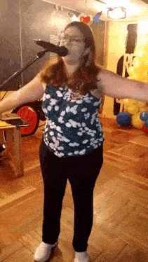 a woman is singing into a microphone with her arms outstretched in front of balloons .