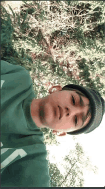 a young man wearing a green shirt and a black hat is taking a selfie