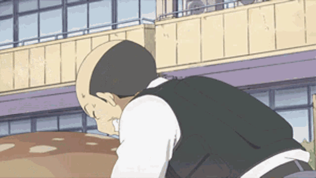 a bald man in a black vest is looking down at something