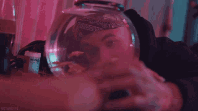 a man with a bandana on his head is smoking a cigarette in front of a fish bowl