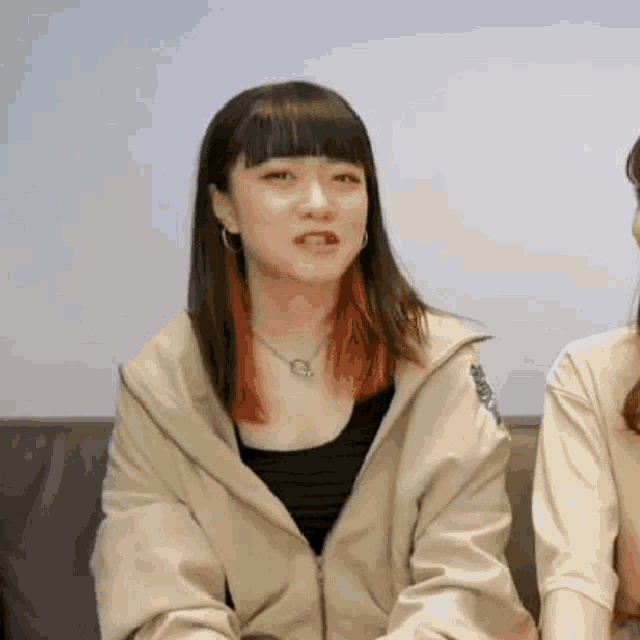 a woman is sitting on a couch making a funny face while another woman looks on .