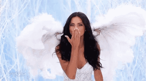 a woman with angel wings is blowing a kiss while wearing a white dress .