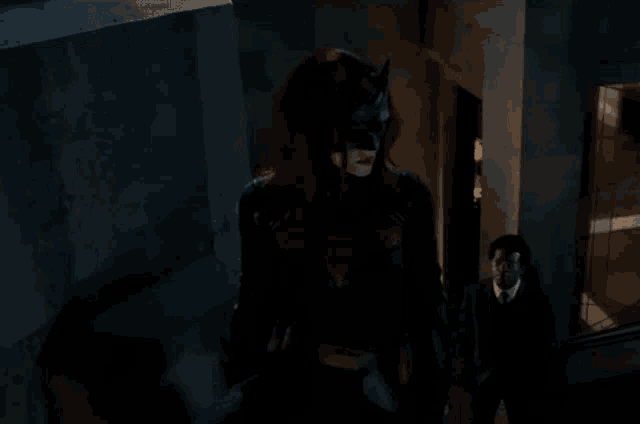 a woman in a batman costume stands next to a man in a suit