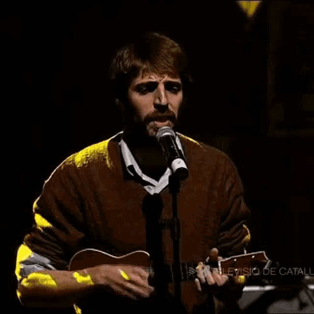 a man singing into a microphone while holding a guitar in front of a sign that says television de catalunya