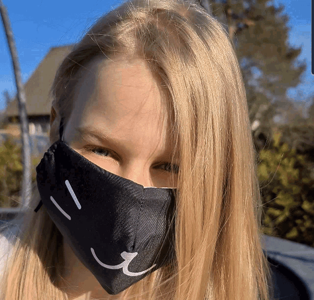 a girl wearing a black face mask with a smiling face drawn on it