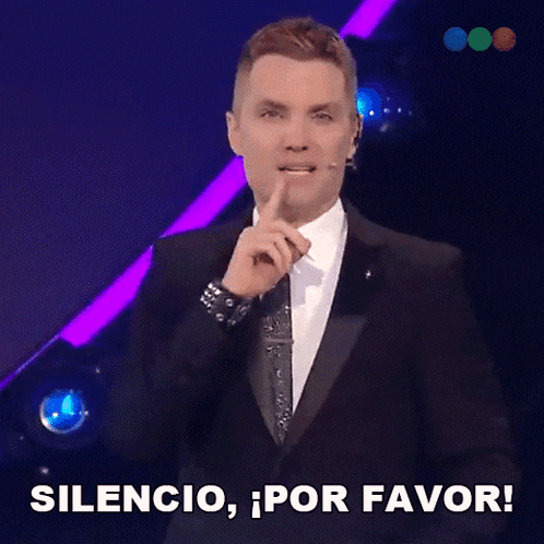 a man in a tuxedo holds his finger to his lips and says silencio