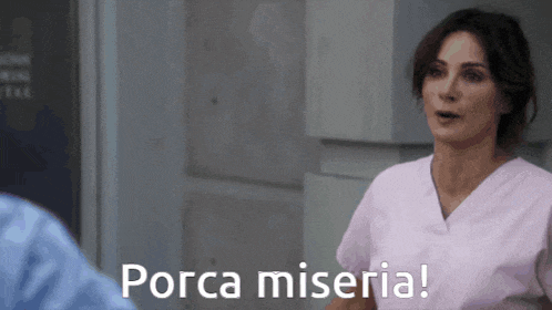 a woman in a pink scrub is talking to a man and says porca miseria