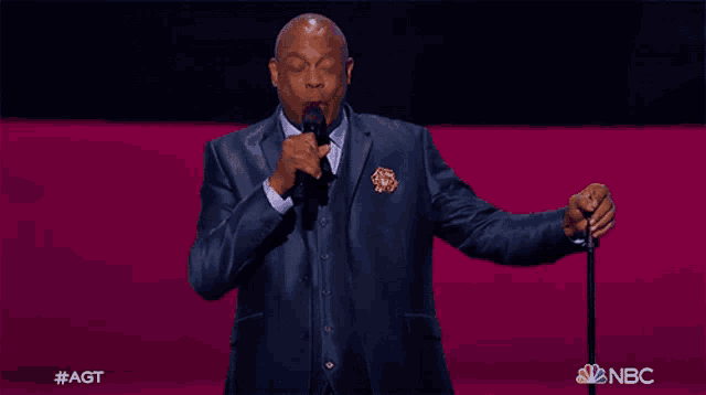 a man in a suit and tie is singing into a microphone with a nbc logo in the corner