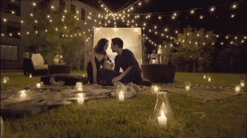 a man and a woman are sitting on a blanket in the grass with candles in front of them .