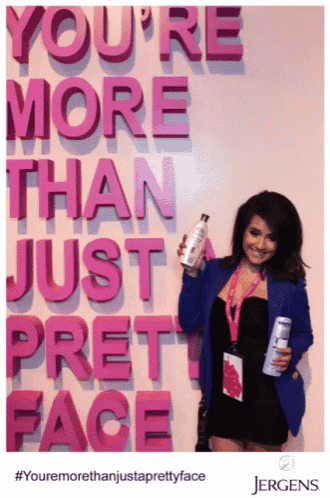 a woman holds a bottle in front of a sign that says you 're more than just pretty face