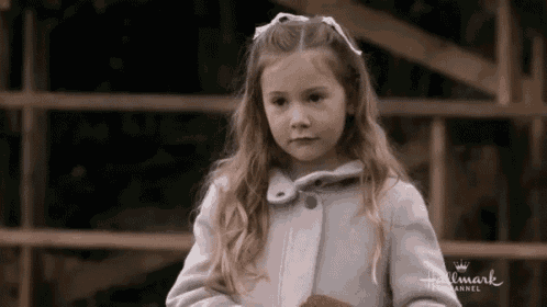 a little girl is wearing a coat and a bow in her hair .