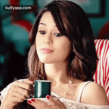 a woman is drinking a cup of coffee while sitting on a couch .