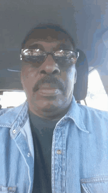 a man with a mustache wearing sunglasses and a denim shirt