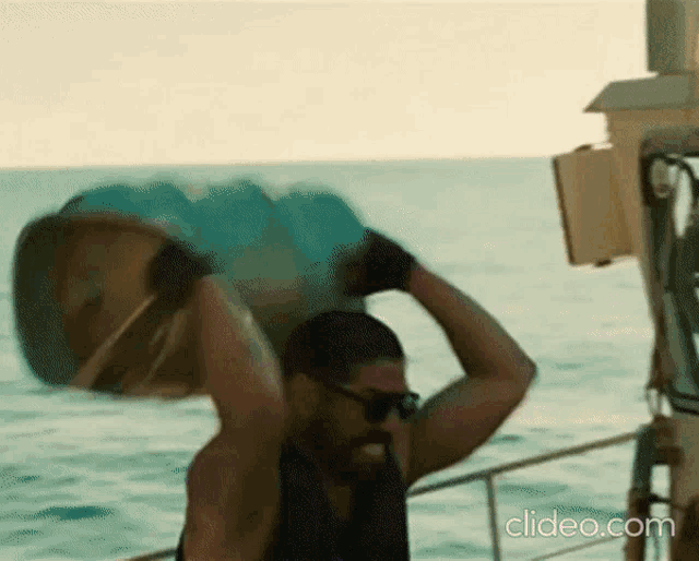a man on a boat is carrying a large item over his head and the website clideo.com is visible in the corner