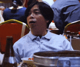 a man in a blue shirt sits at a table with a bowl of food