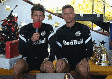 two men sitting next to each other wearing red bull shirts