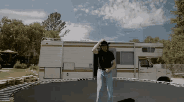 a man in a cowboy hat stands on a trampoline in front of a camper van