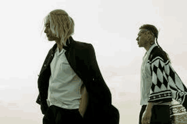 two men are standing next to each other in front of a cloudy sky .