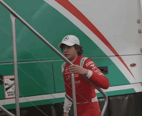 a man wearing a red and white mercedes racing suit is standing on a set of stairs