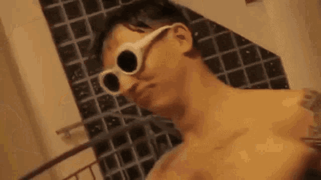 a shirtless man wearing sunglasses is taking a picture of himself in a bathroom .