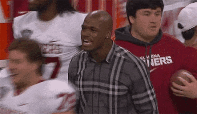 a man in a plaid shirt with oklahoma written on his shirt is holding a football