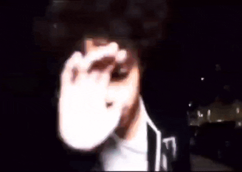 a man with curly hair is covering his face with his hands while wearing a hoodie with the letter w on it .