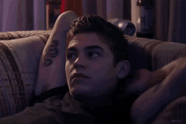 a man with a tattoo of a snake on his arm is laying on a couch