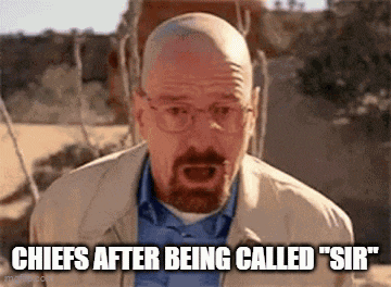 a bald man with a beard and glasses is standing in the desert and talking .