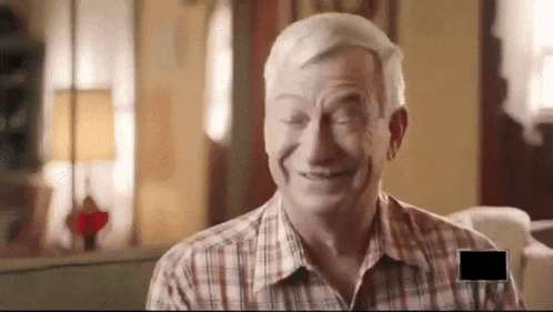 an elderly man in a plaid shirt is smiling with a black square in the corner